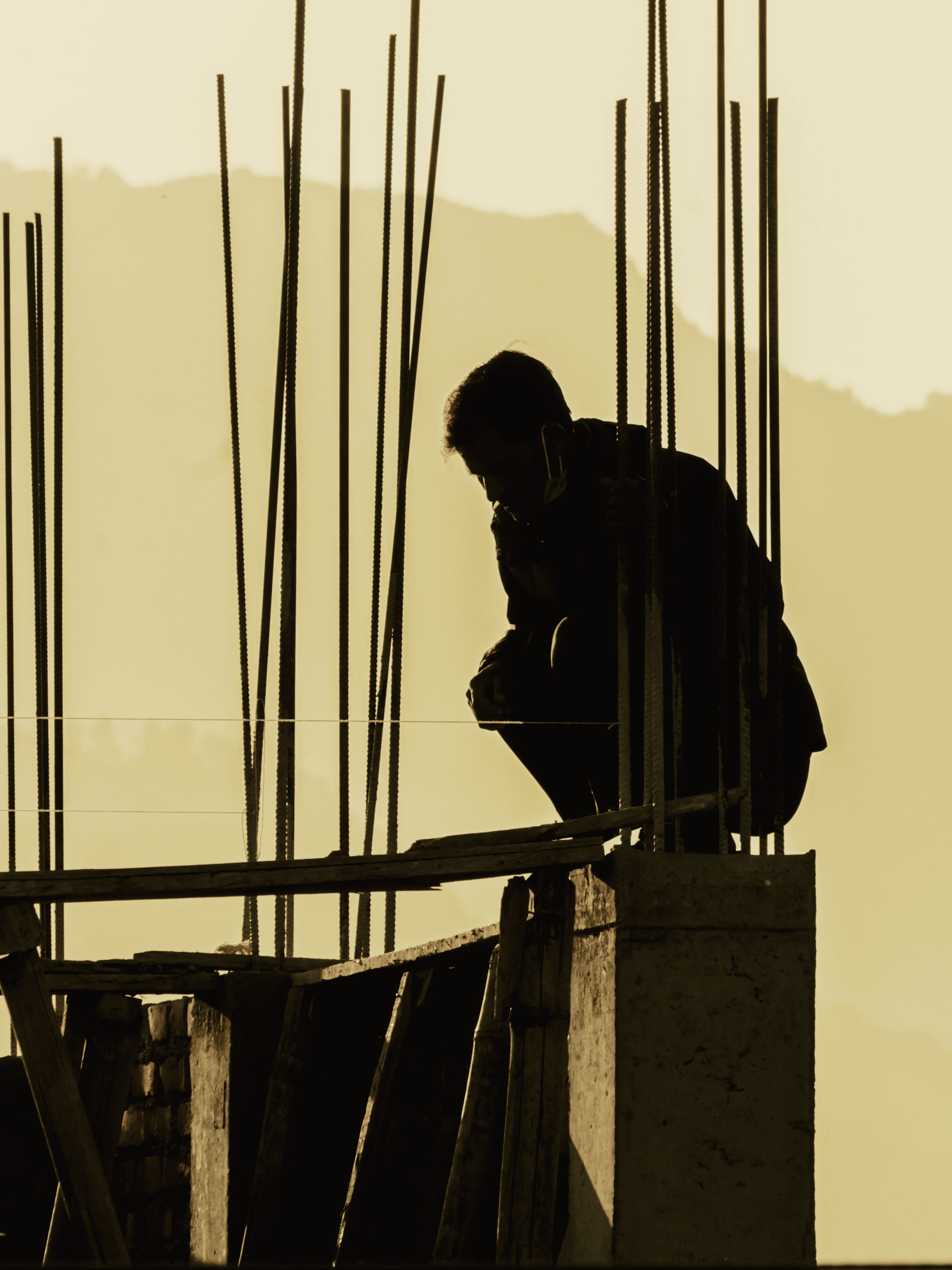 A construction worker crouched among rebar against a golden sunset