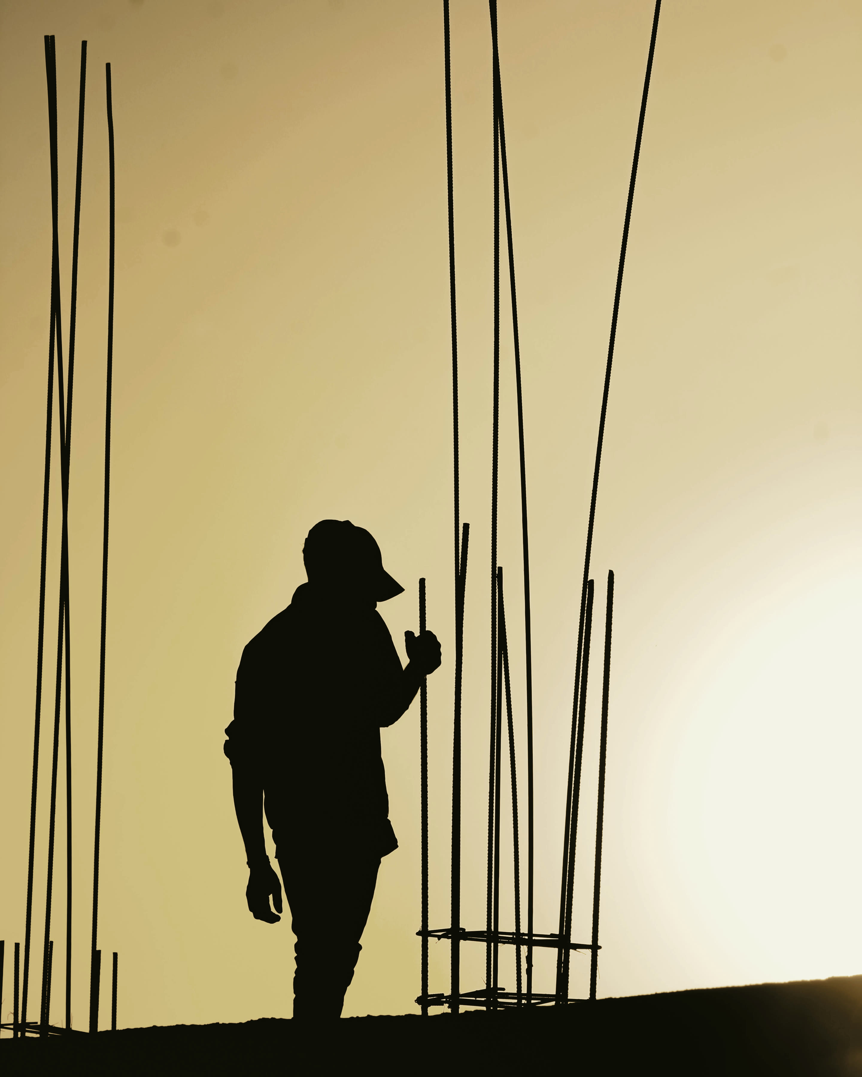 A construction worker silhouetted among rebar against a golden sunset