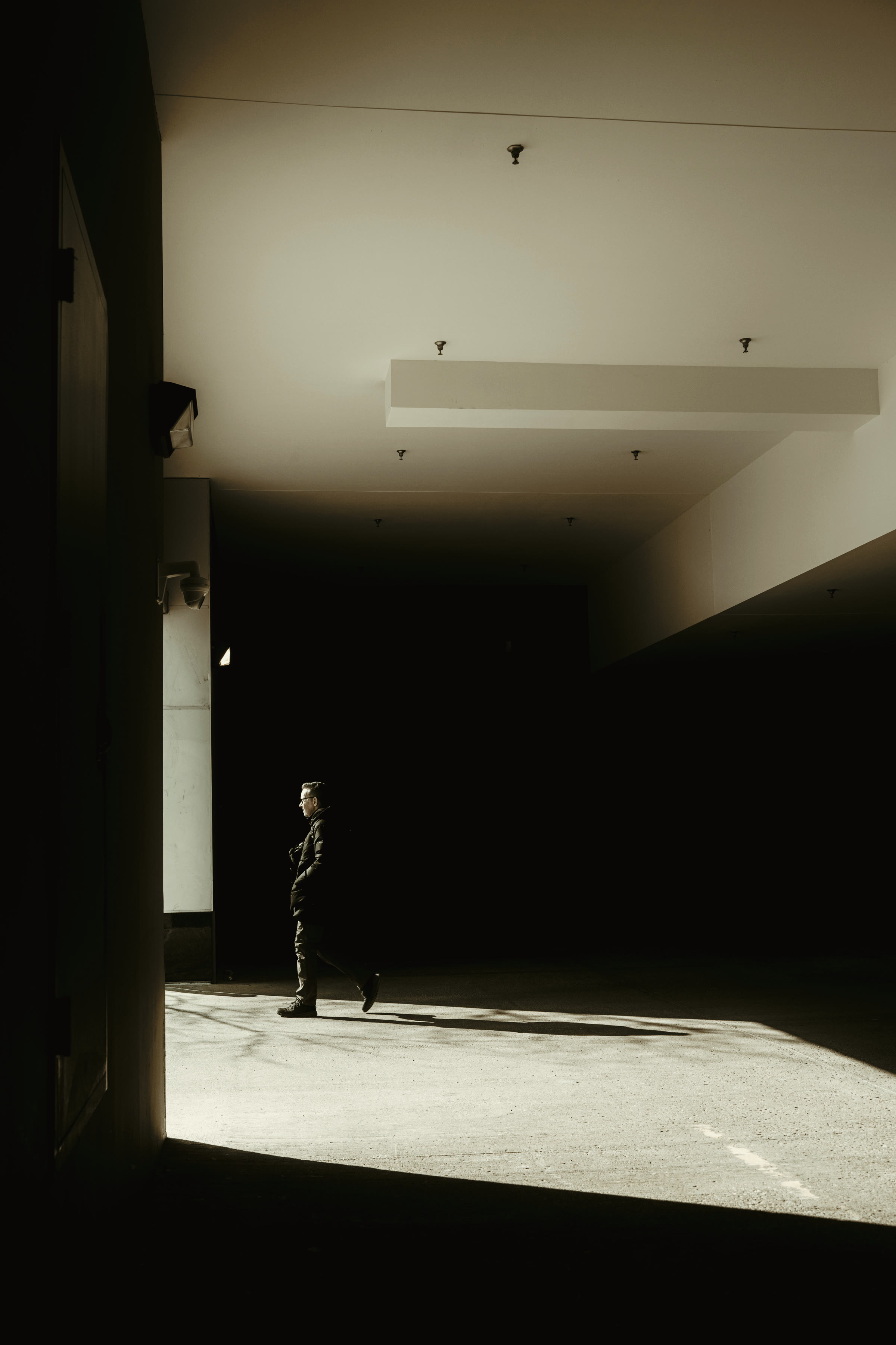 A lone figure walking through a vast concrete hall lit by a single shaft of light